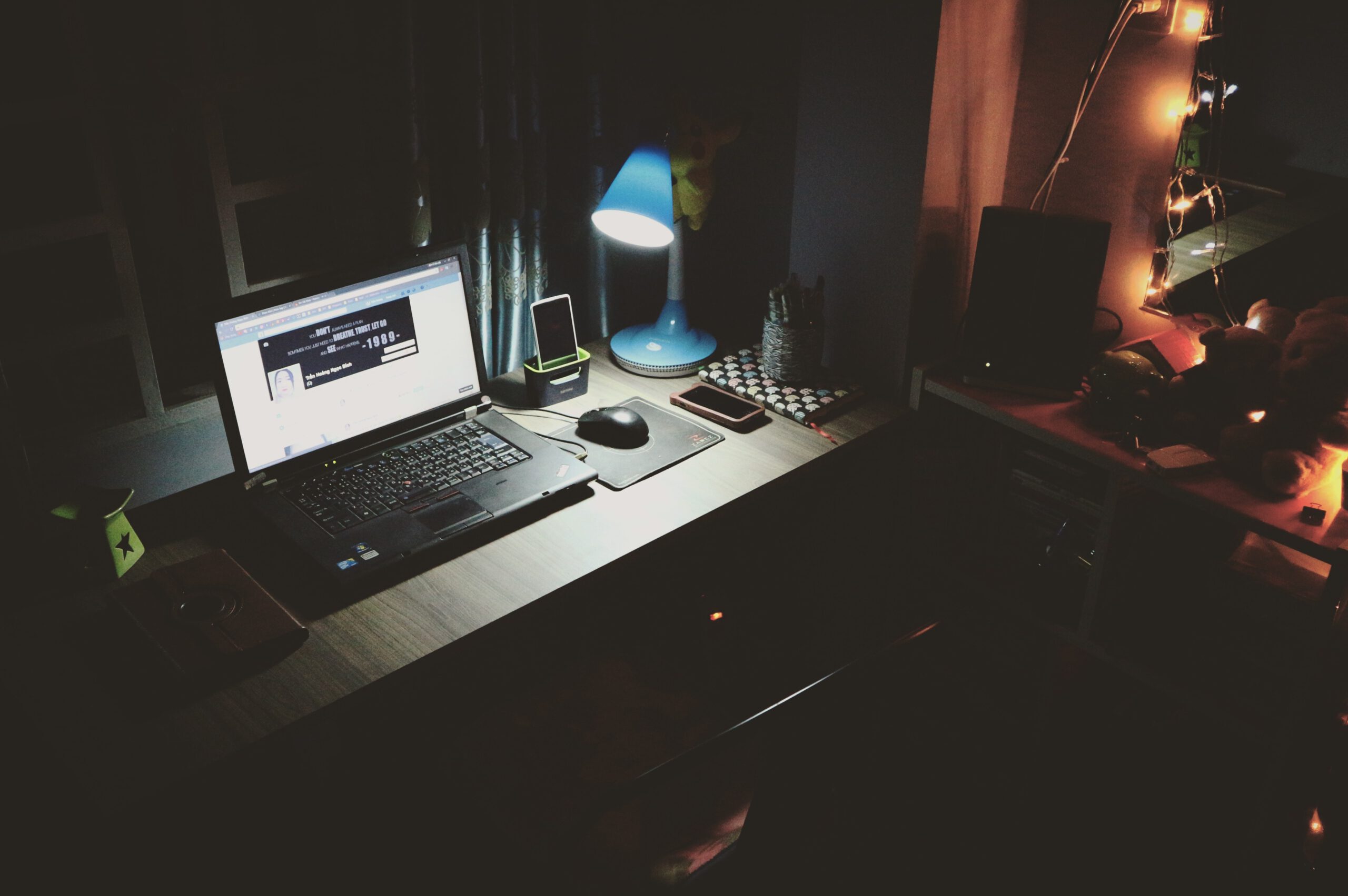 Biurko z otwartym laptopem, świecącą się lampką i drobnymi przedmiotami noca
