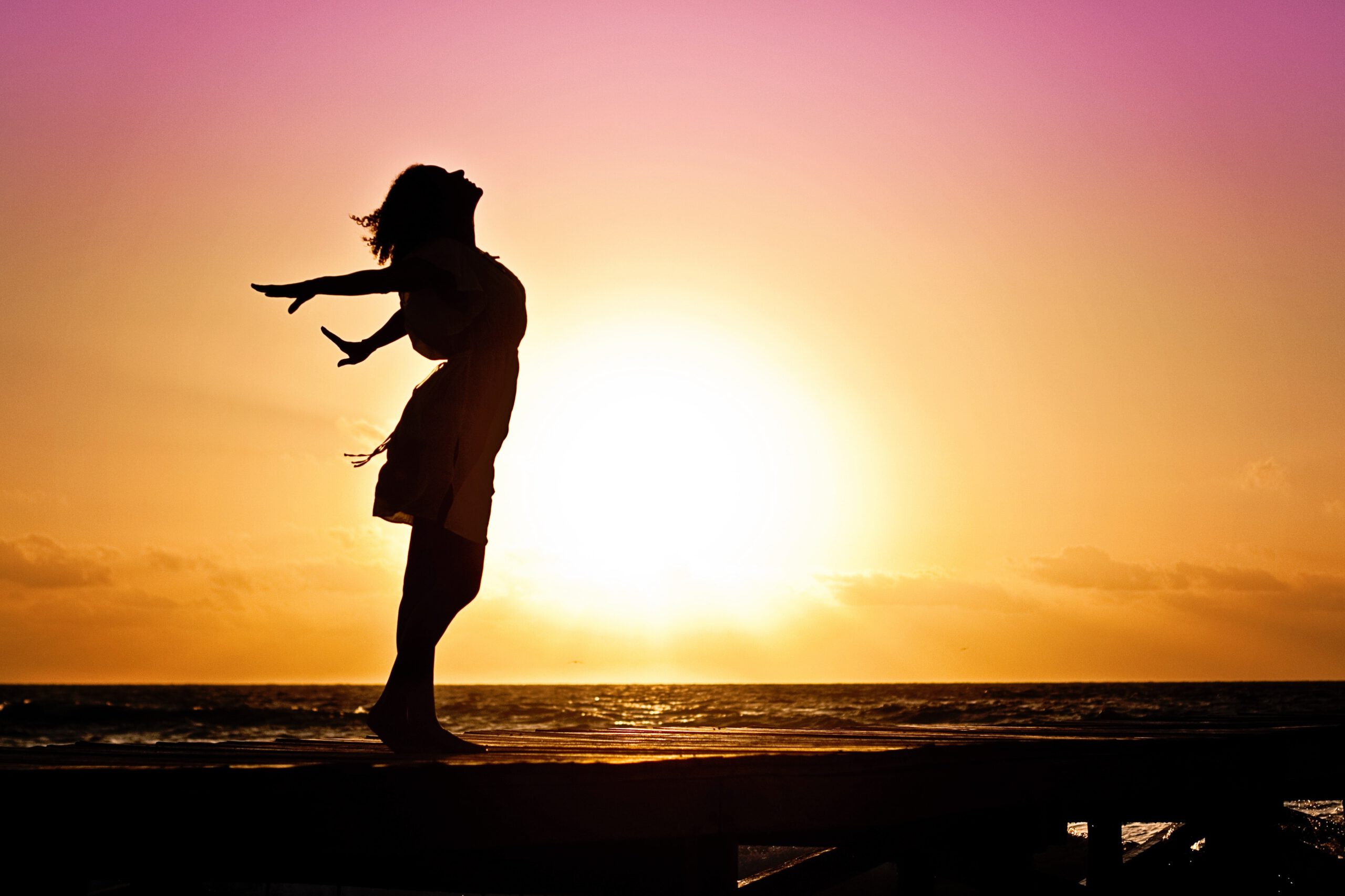 Kobieta pozująca nad morzem na tle zachodzącego słońca