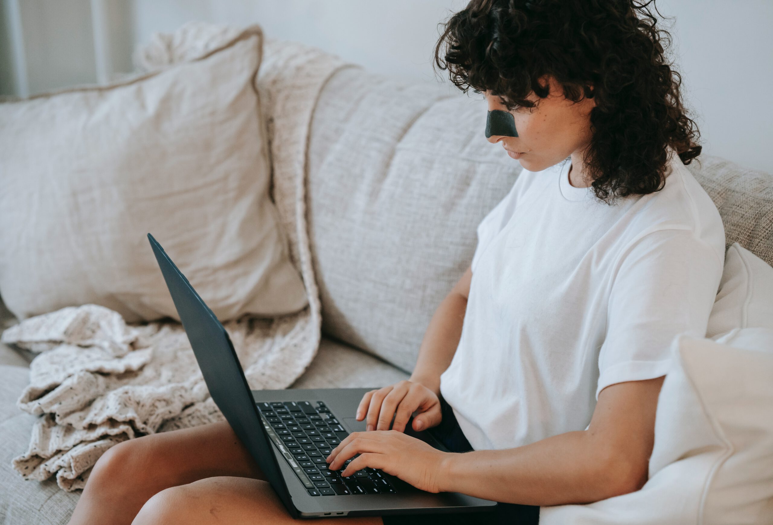Kobieta siedząca na kanapie z laptopem na kolanach i czarnym plasterkiem na wągry na nosie