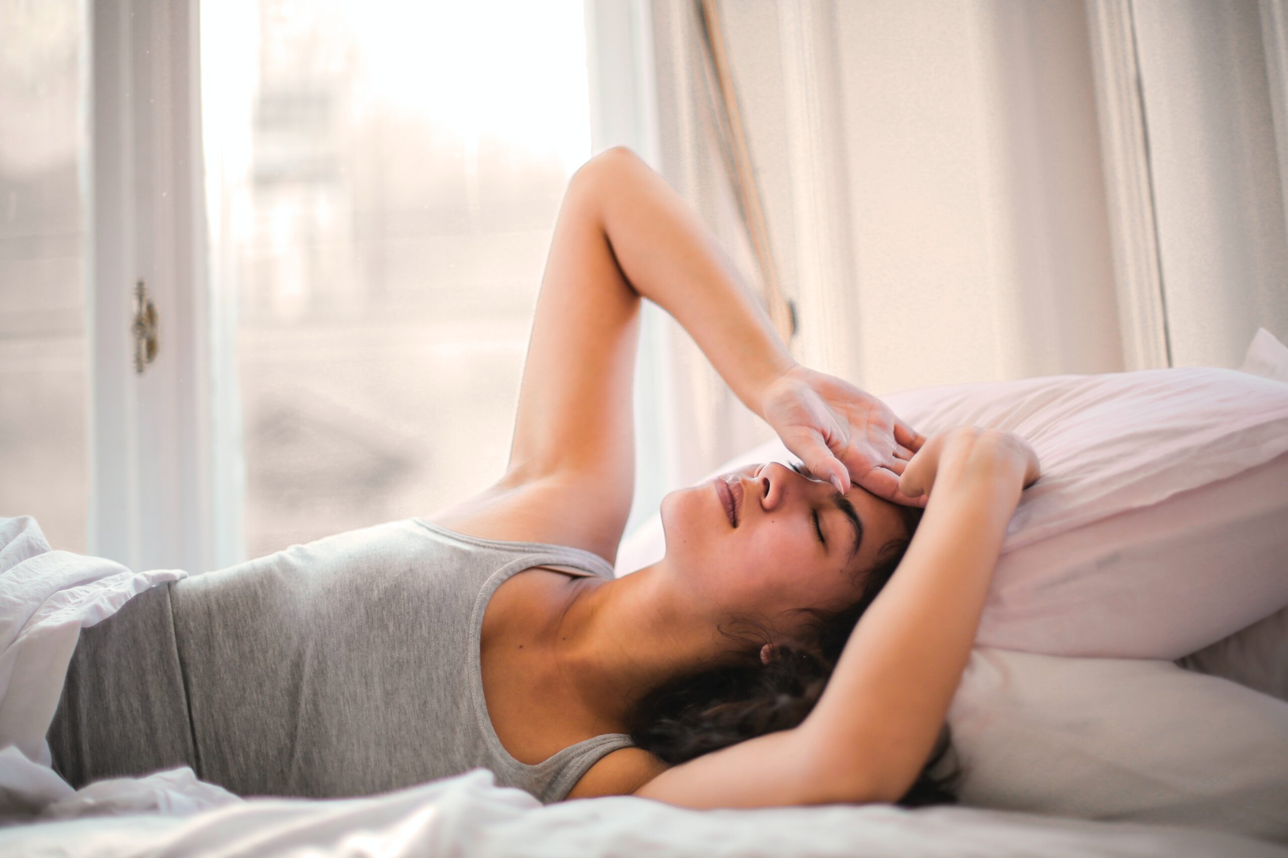 Kobieta z bólem i urazy głowy leżąca w łóżku z dłonią na czole