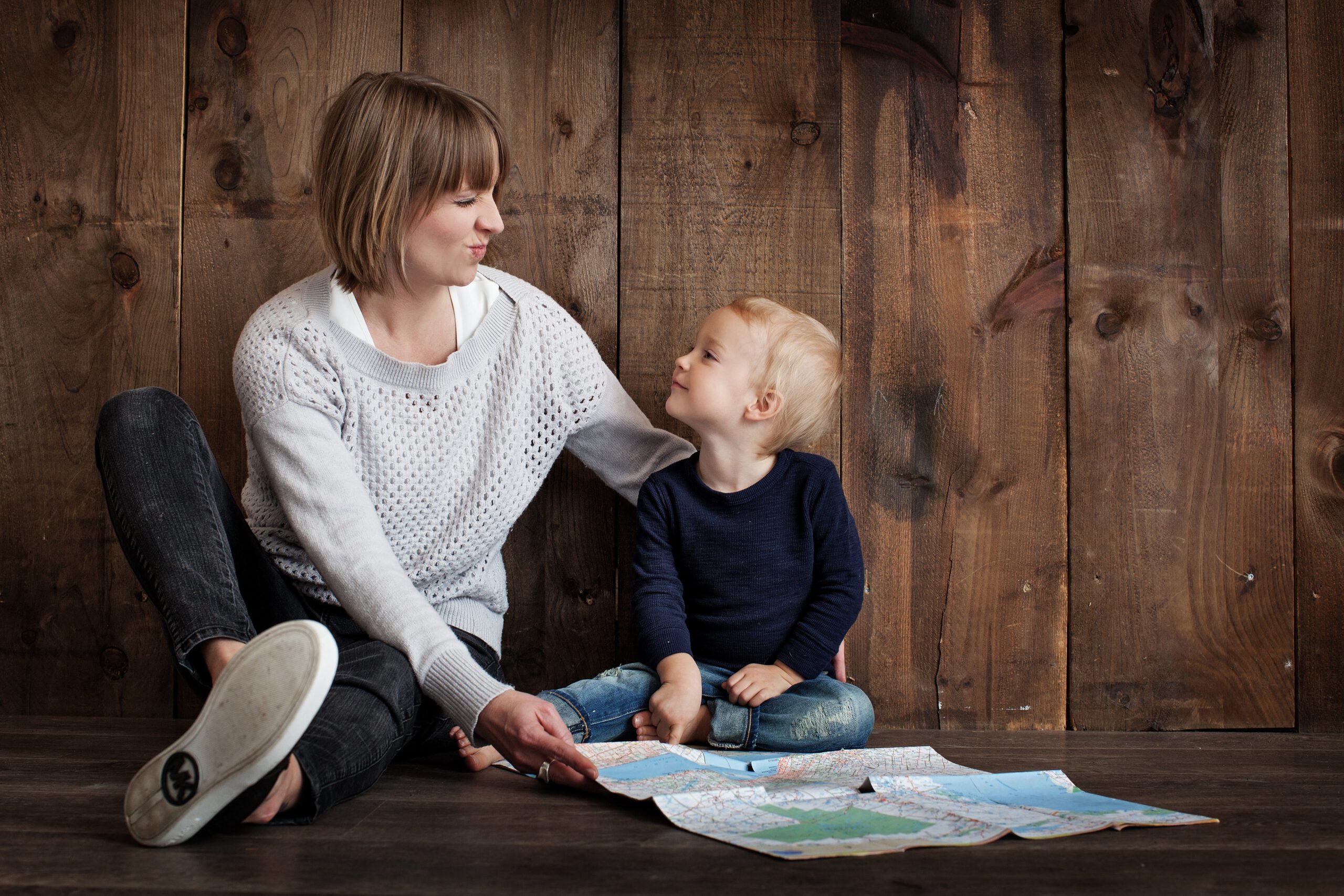 Mały chłopczyk z mamą siedzący na tle drewnianej ściany z papierową mapą