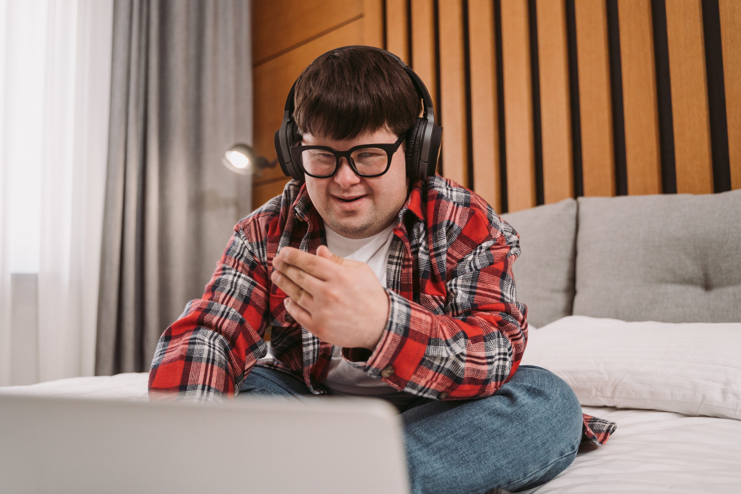Mężczyzna z upośledzeniem umysłowym siedzący na łóżku z laptopem i słuchawkami na uszach
